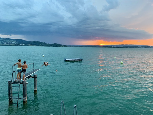 Kinder springen vom Sprungturm in den Zugersee bei Sonnenuntergang